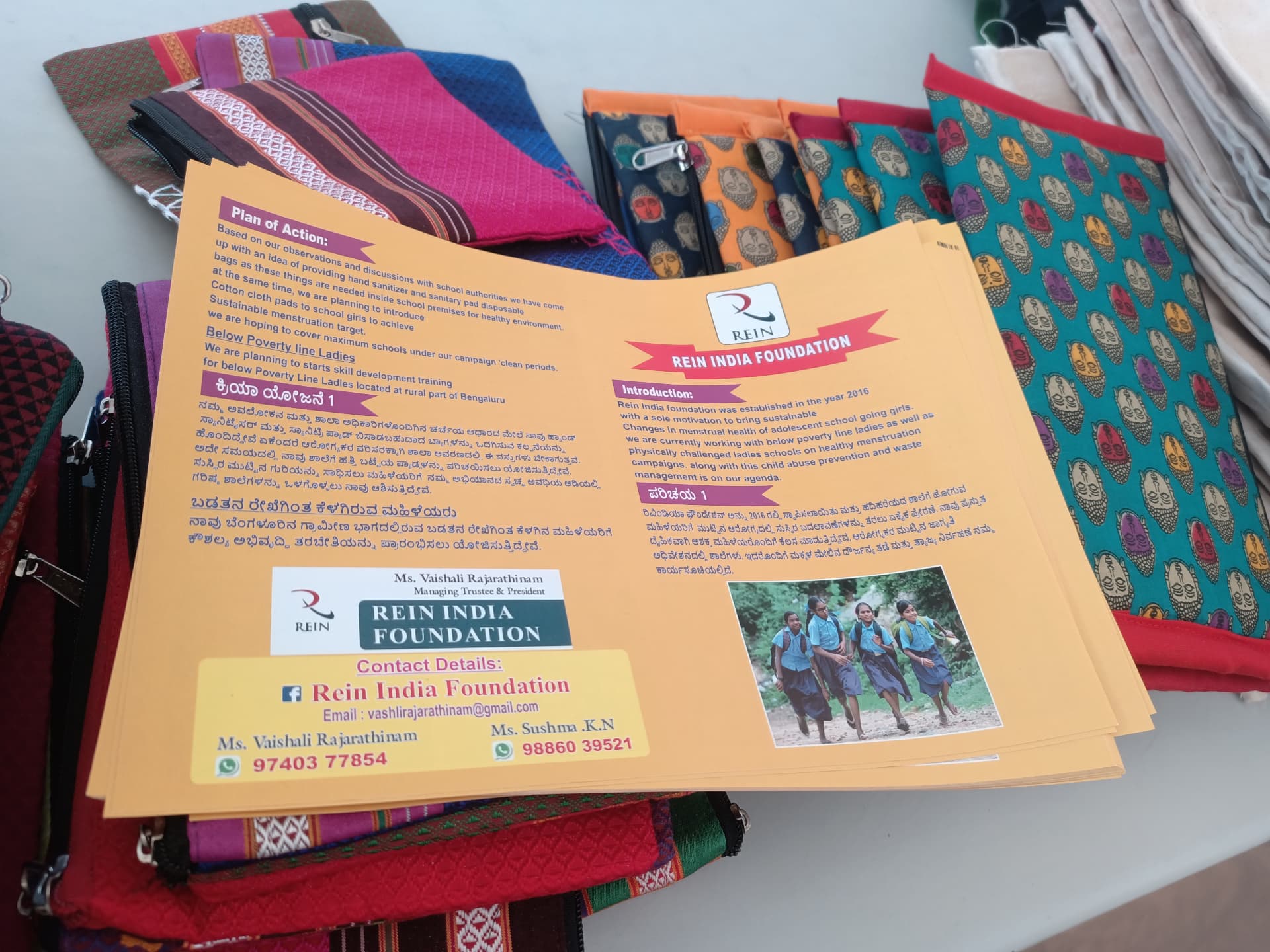 REIN India Foundation brochure beside handcrafted pouches and cotton bags
